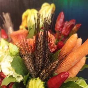 Dettaglio macro bouquet vegano con carote fresche, spighe di grano scure e fiori di zucca